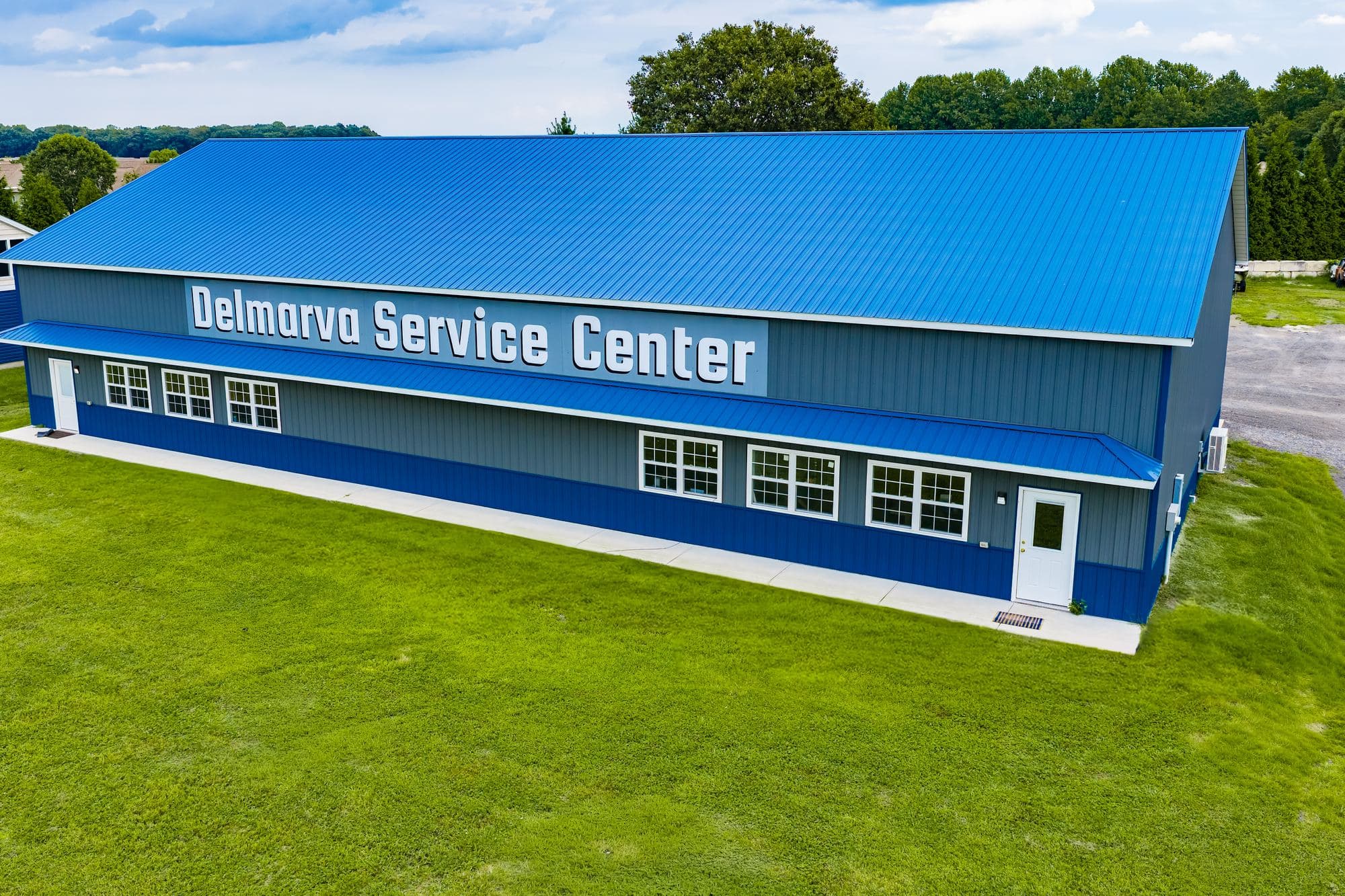 Aerial view of the Delmarva Service Center building in Milton, Delaware — blue metal roof, Delmarva Service Center sign across the facade, and mowed lawn on Harbeson Road