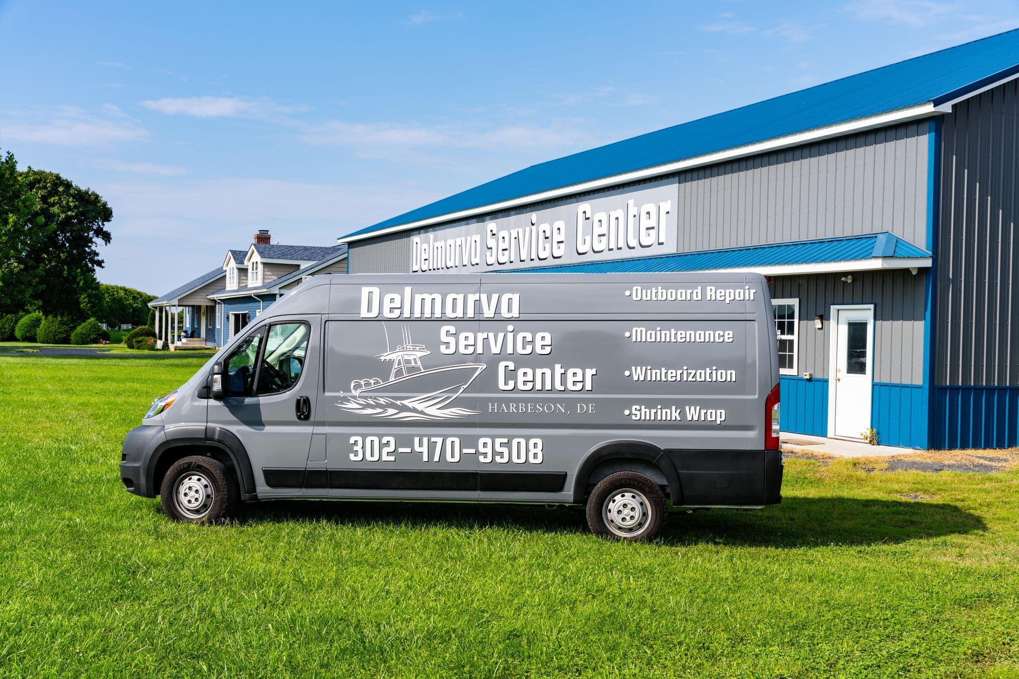 Delmarva Service Center's mobile service van — lettered for outboard repair, maintenance, winterization, and shrink wrap — parked in front of the shop's signed building on Harbeson Road