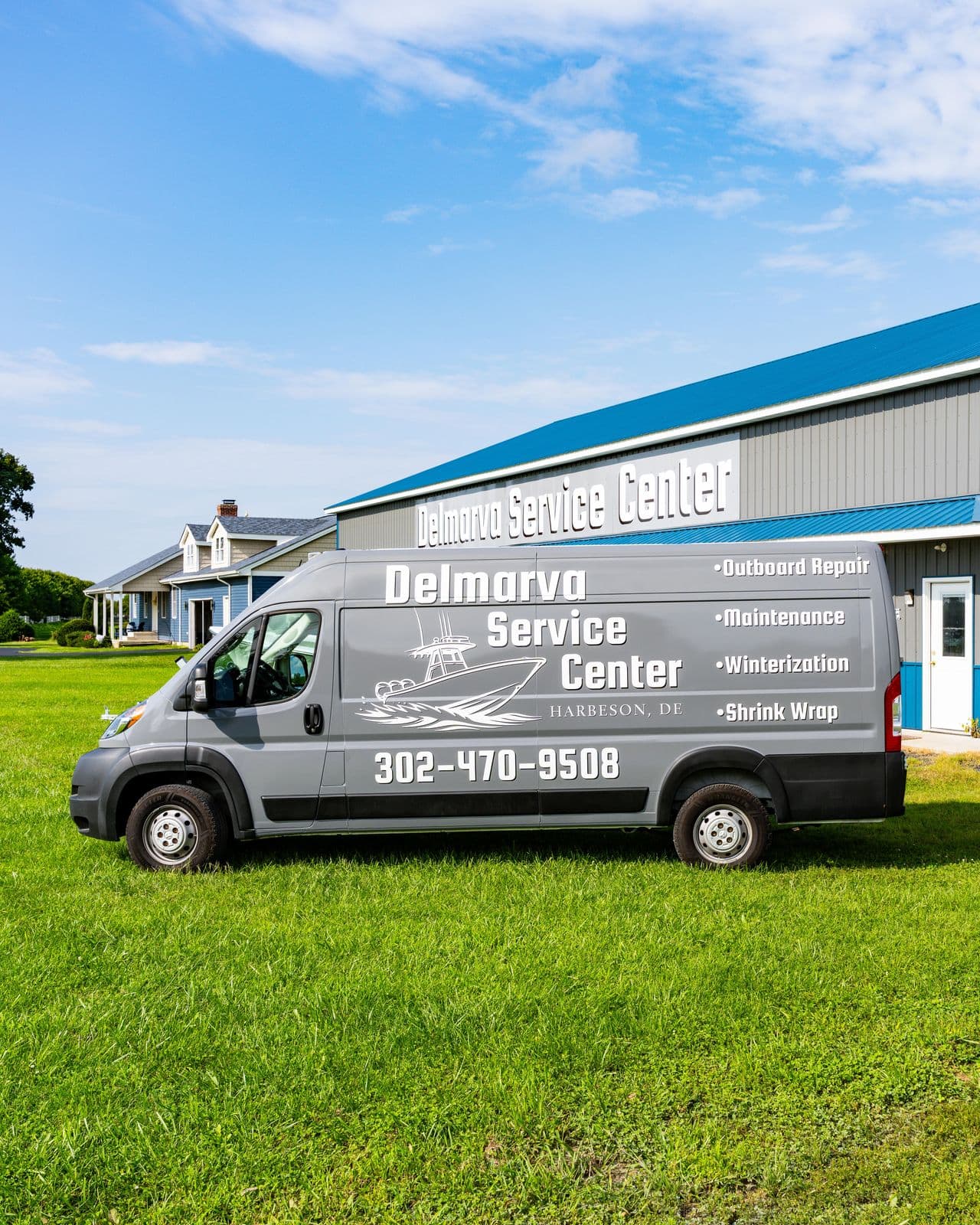 The grey Delmarva Service Center service van parked on the lawn beside the blue-roofed shop at 18473 Harbeson Road, Milton, Delaware